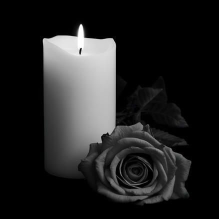 Eine brennende, weiße Kerze. Davor eine Rose. Das Bild ist schwarz-weiß